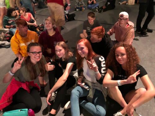 Teenagers sitting together at a Christian youth event, making peace signs and smiling.